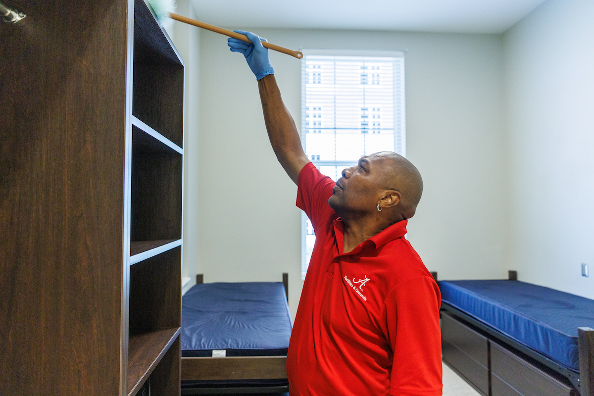 U A facilities staff cleaning top of bookcase 