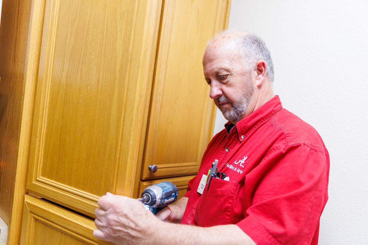 U A facilities staff repairing cabinet door