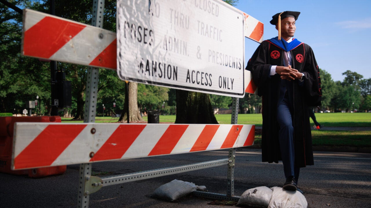 Sunday Okafor wearing graduation regalia and standing near road construction signage