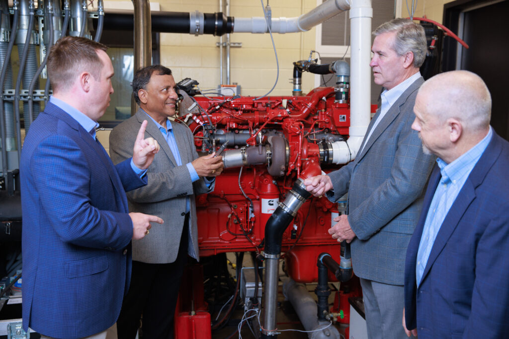 Dr. Joshua Bittle, Dr. Ajay Agrawal, Alabama Port Authority Director John C. Driscoll, and Tim Haskew, Associate Dean for Research, College of Engineering at the diesel combustion lab. Dr. Agrawal holds a small engine component.