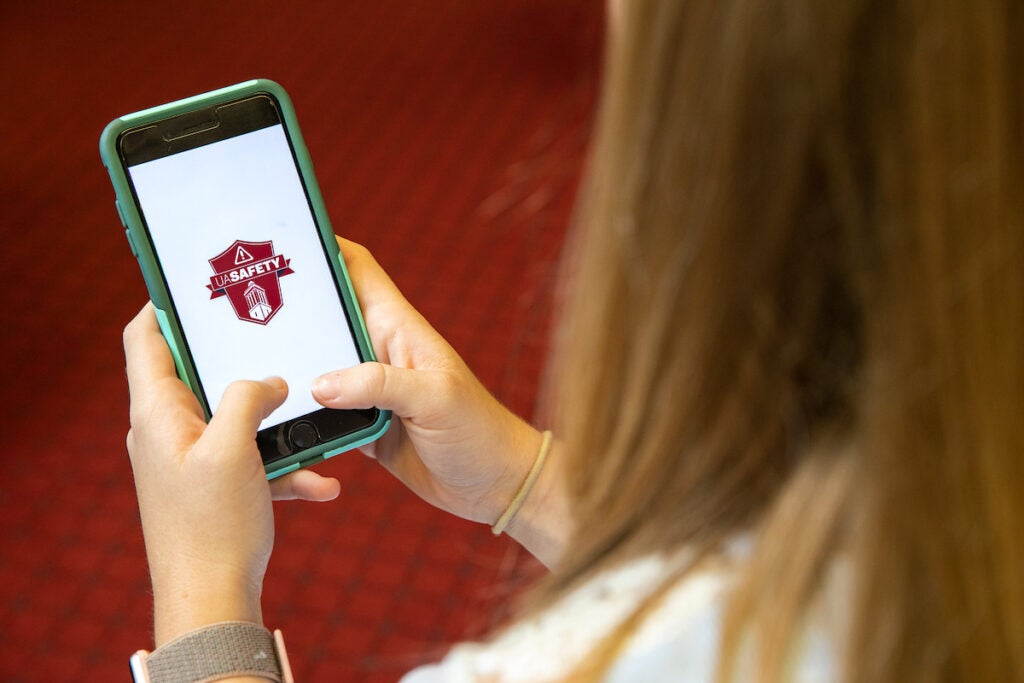 A girl holding a cell phone with the UA Safety app displayed on the screen.