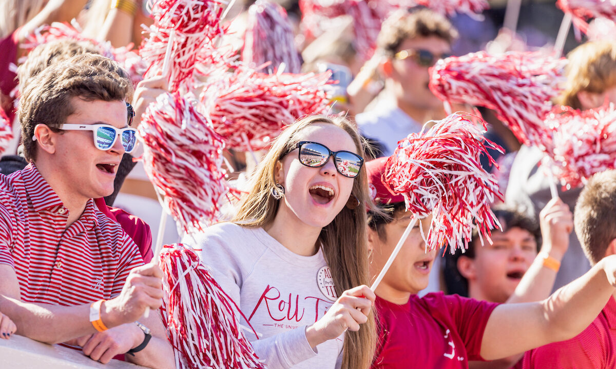 A group of fans cheering for the Alabama Crimson Tide.