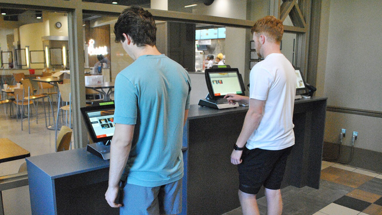 Two male students order food from a kiosk.