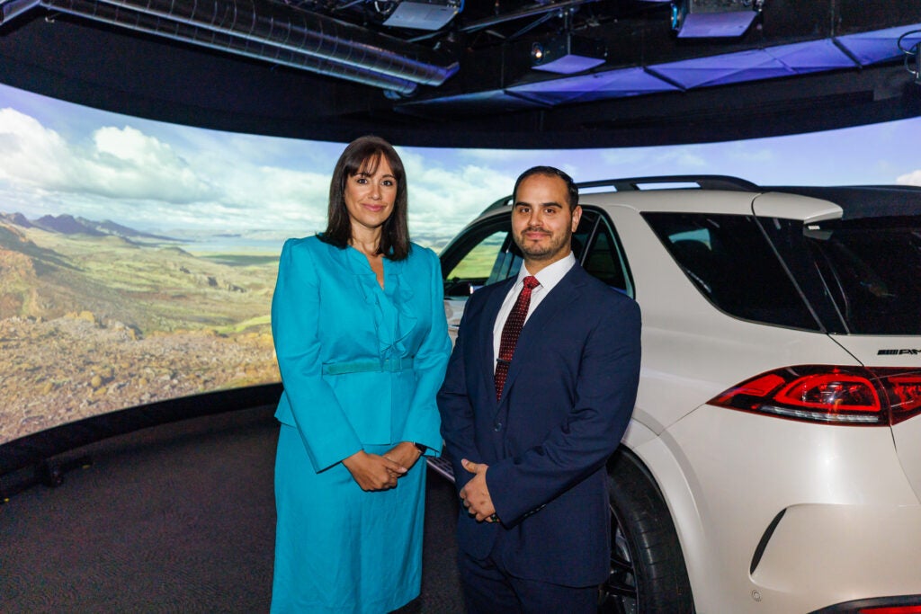 Dr. Despina Stavrinos and Dr. Ben McManus stand in front of the TRIP lab driving simulator. 