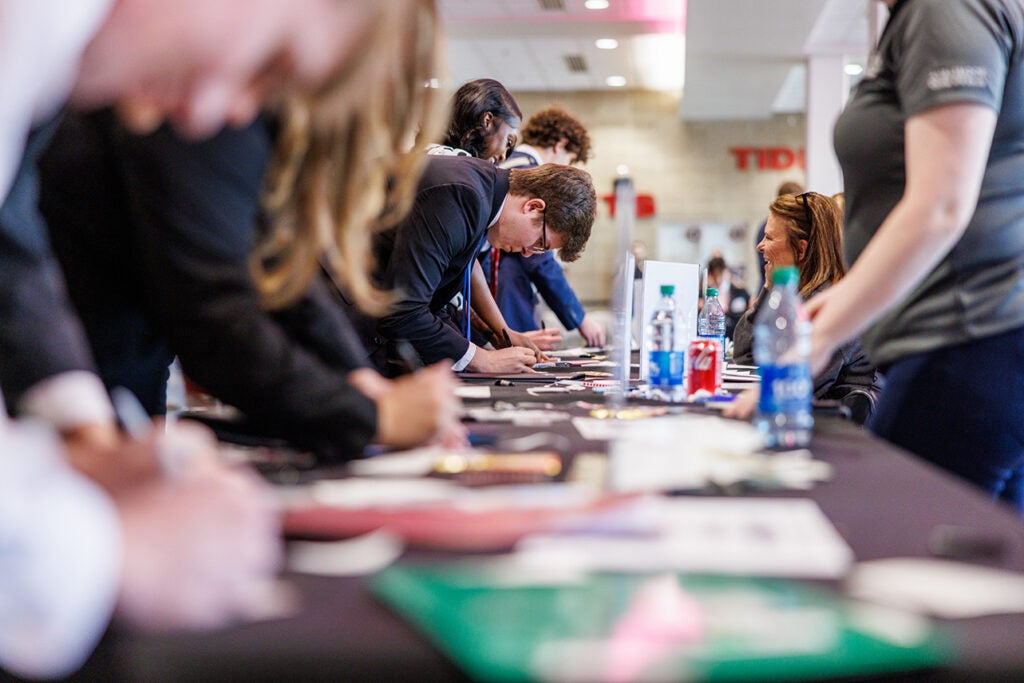 Various students fill out paperwork at multiple tables.