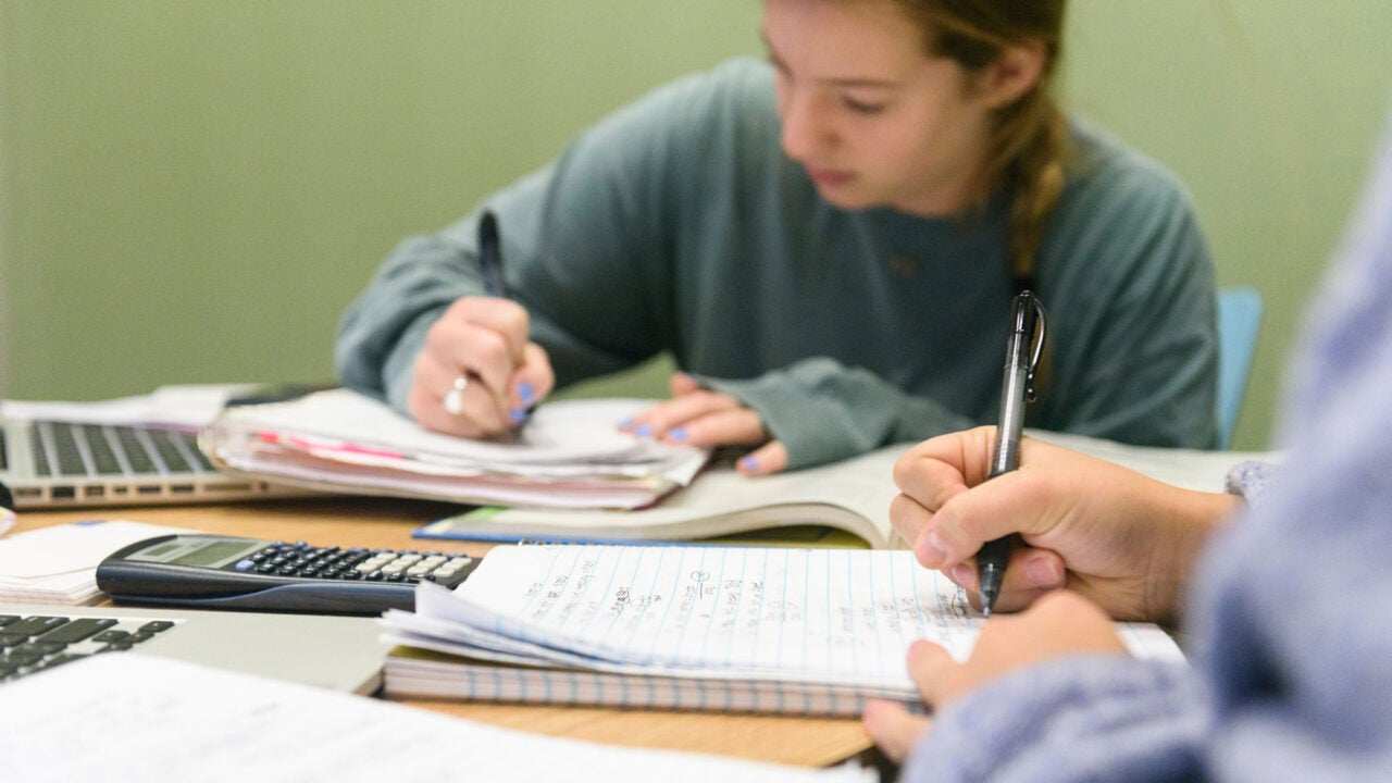 closeup of a a table full of notebooks where two young women are studying