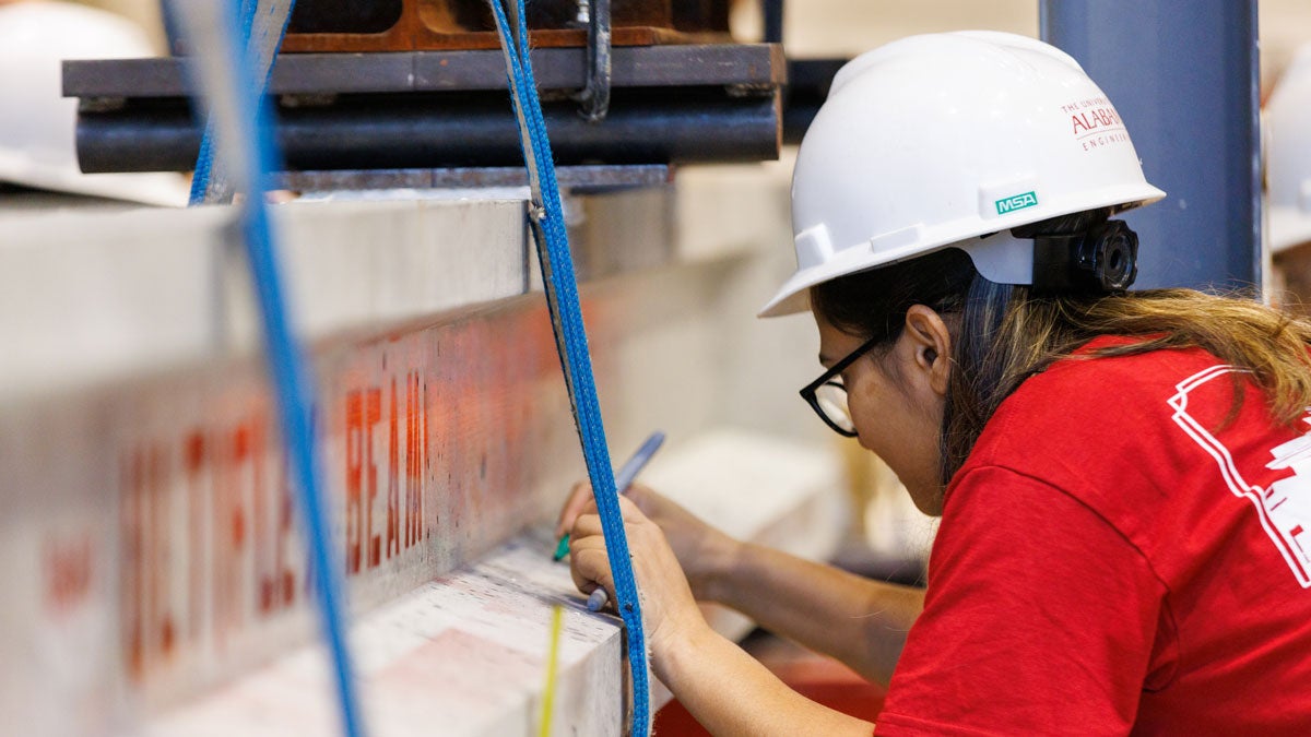 student wearing a hard hat writes on a concrete beam