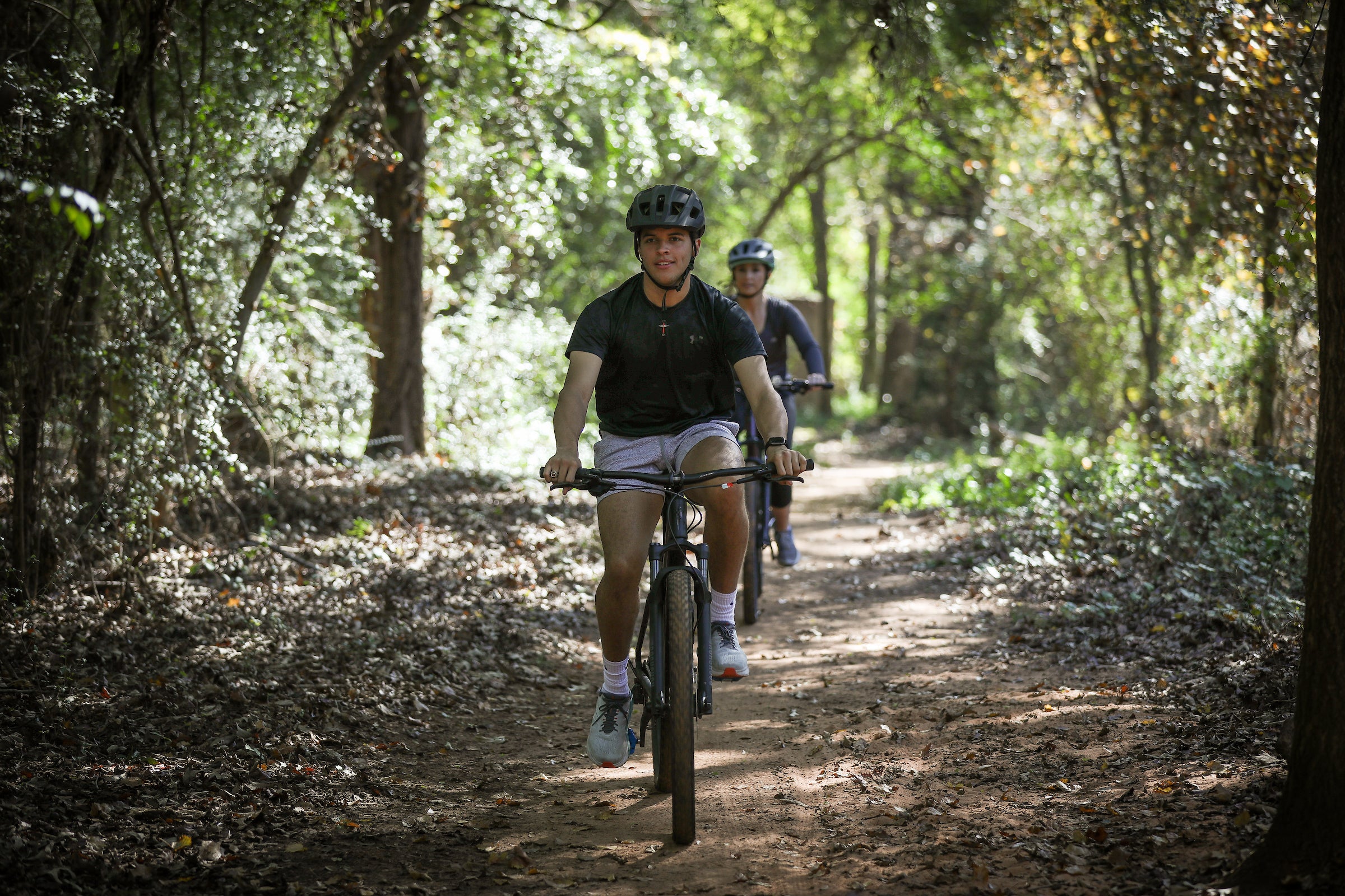 two young people riding bikes on a shady nature trail