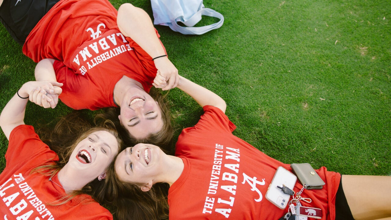 three young women lying on the grass with their heads together