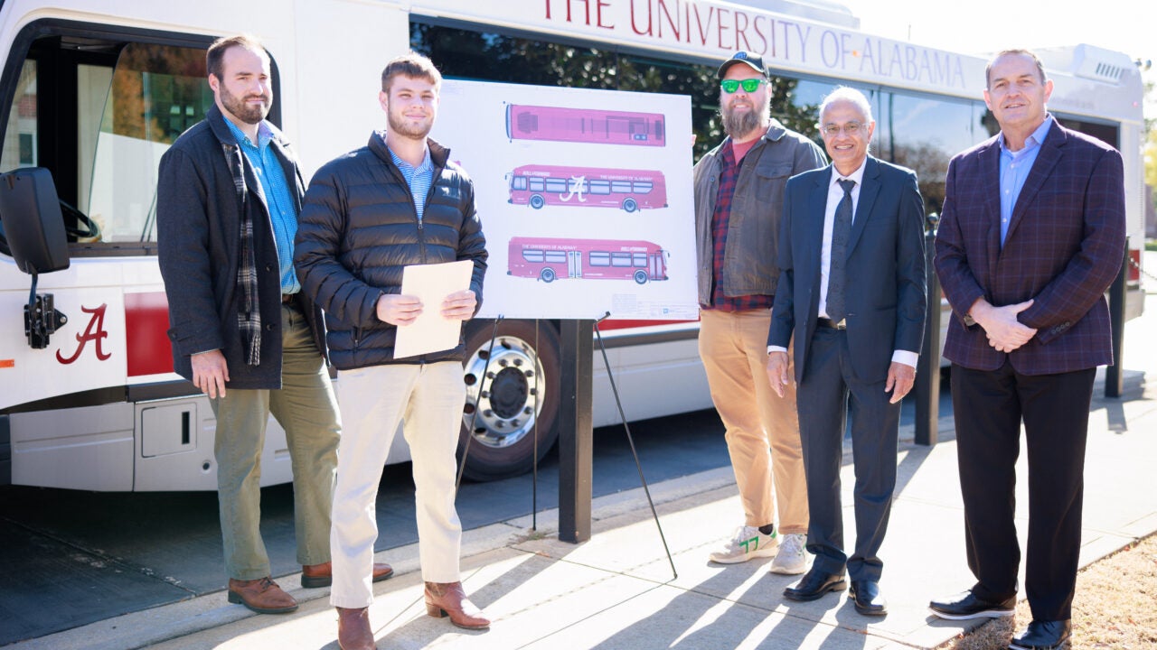 Winners and faculty members stand in front of a Crimson bus