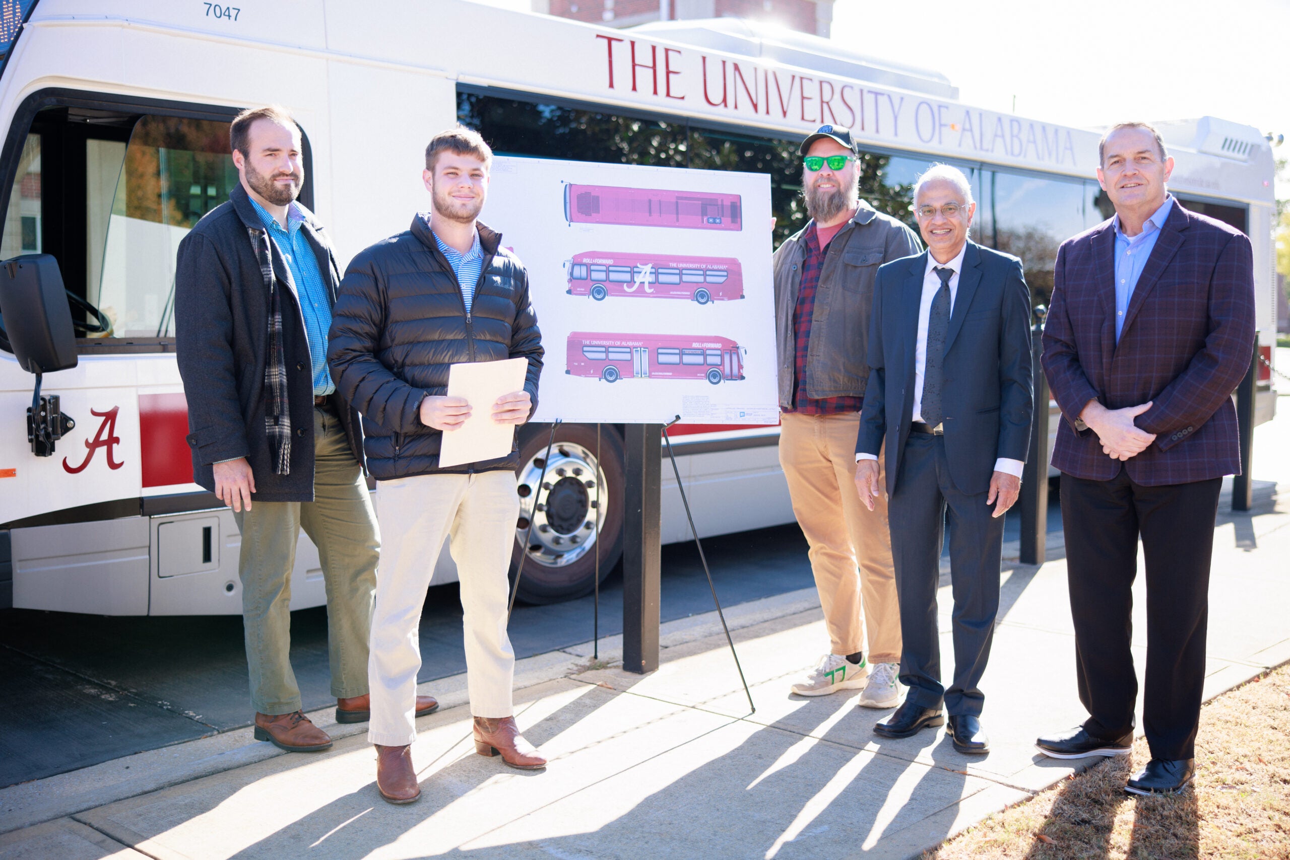 Winners and faculty members stand in front of a Crimson bus