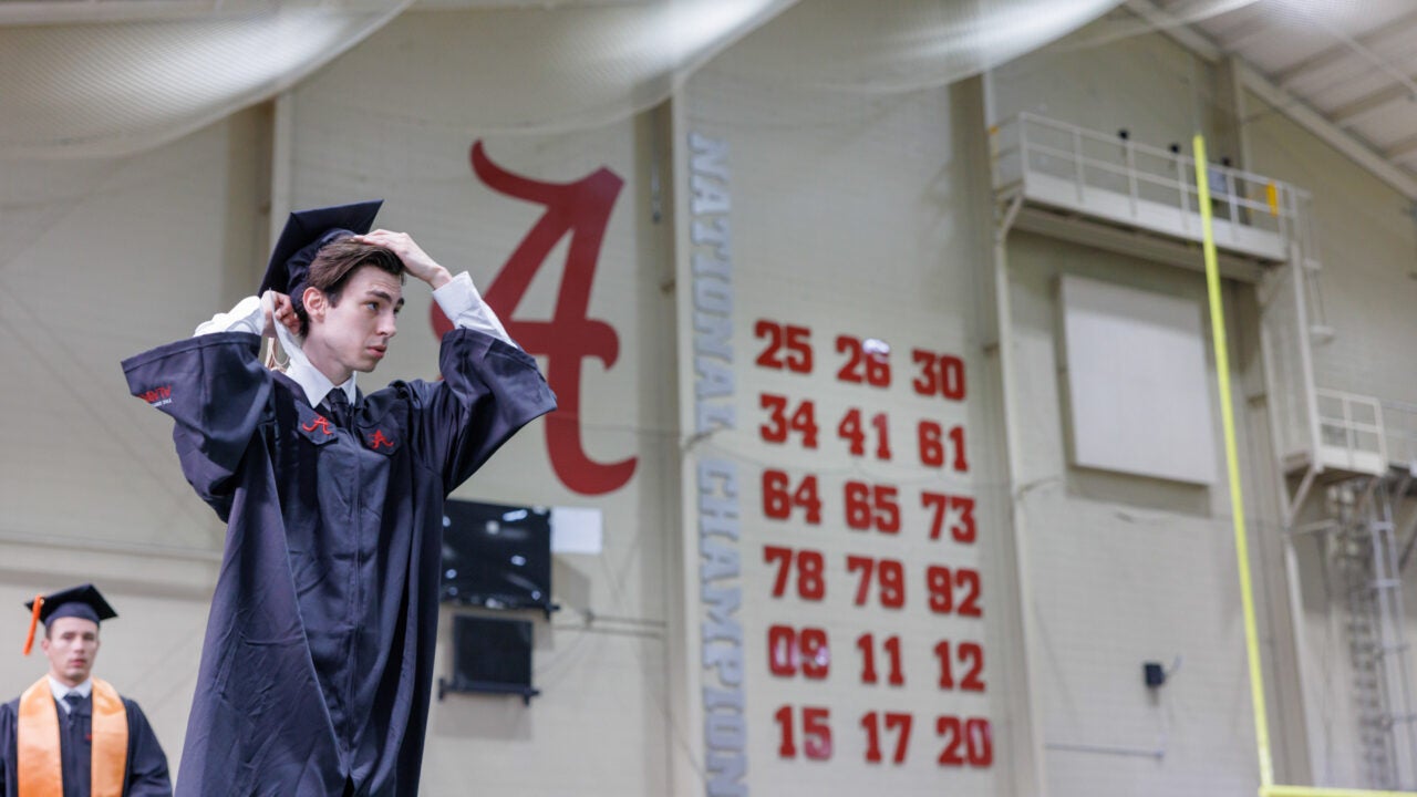 a young man adjusts his hat before lining up for commenement