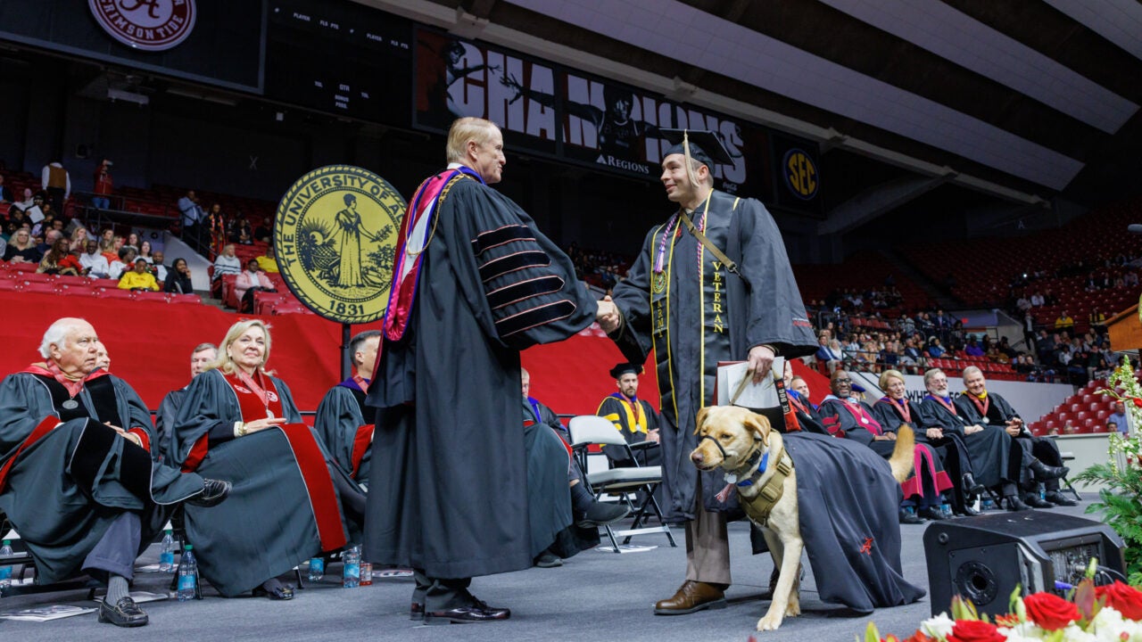 Dr. Bell congratulates a new grad, who stands on stage with a service dog.