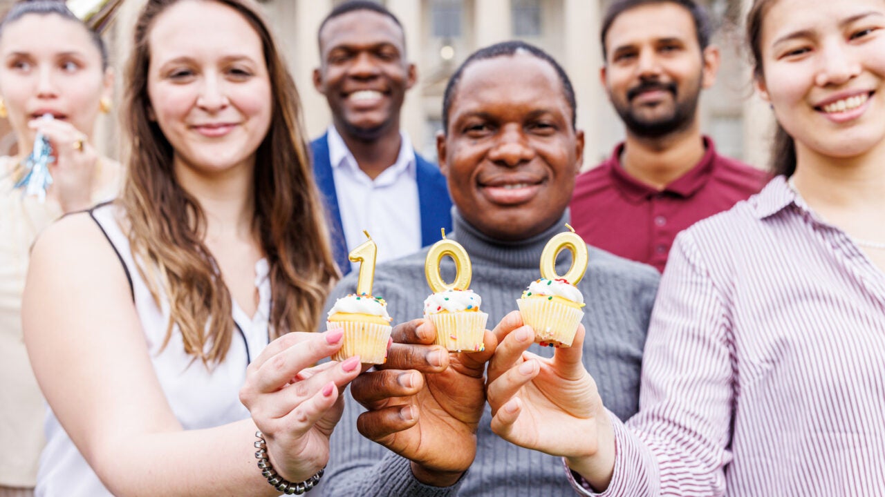 Graduate students holding cupcakes with candles displaying 100