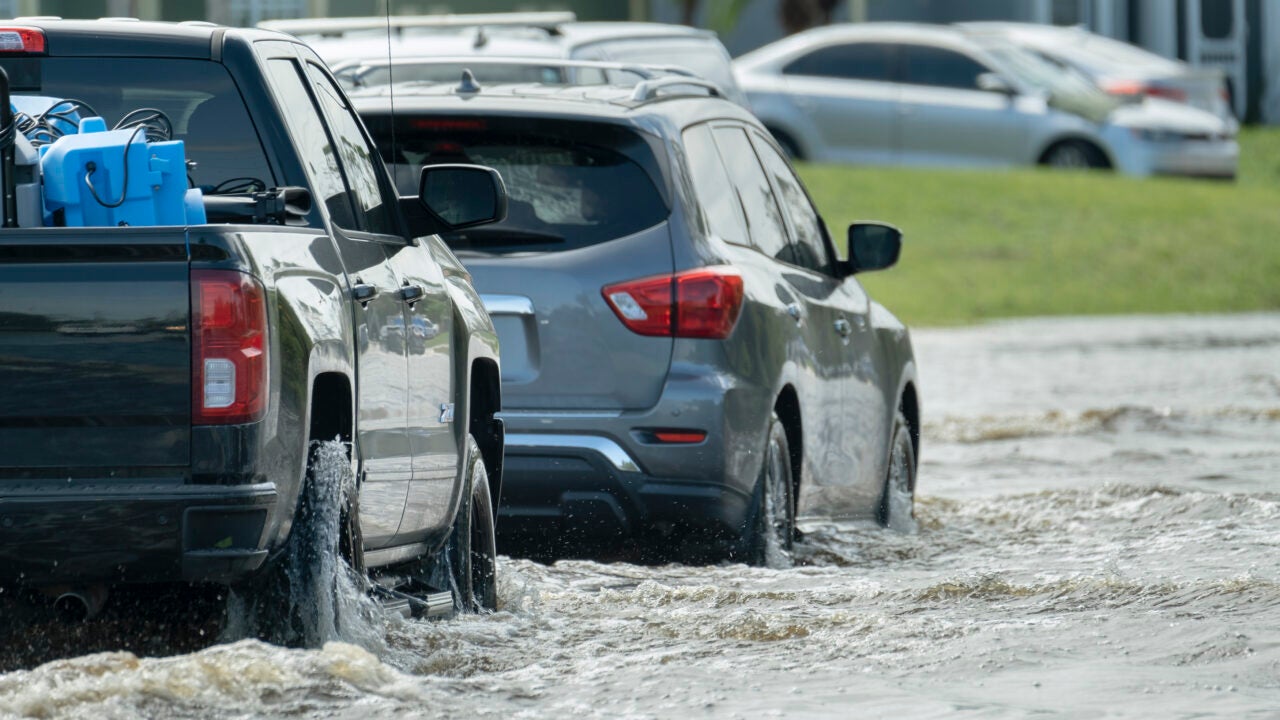 A flooded road with cars trying to drive through it.