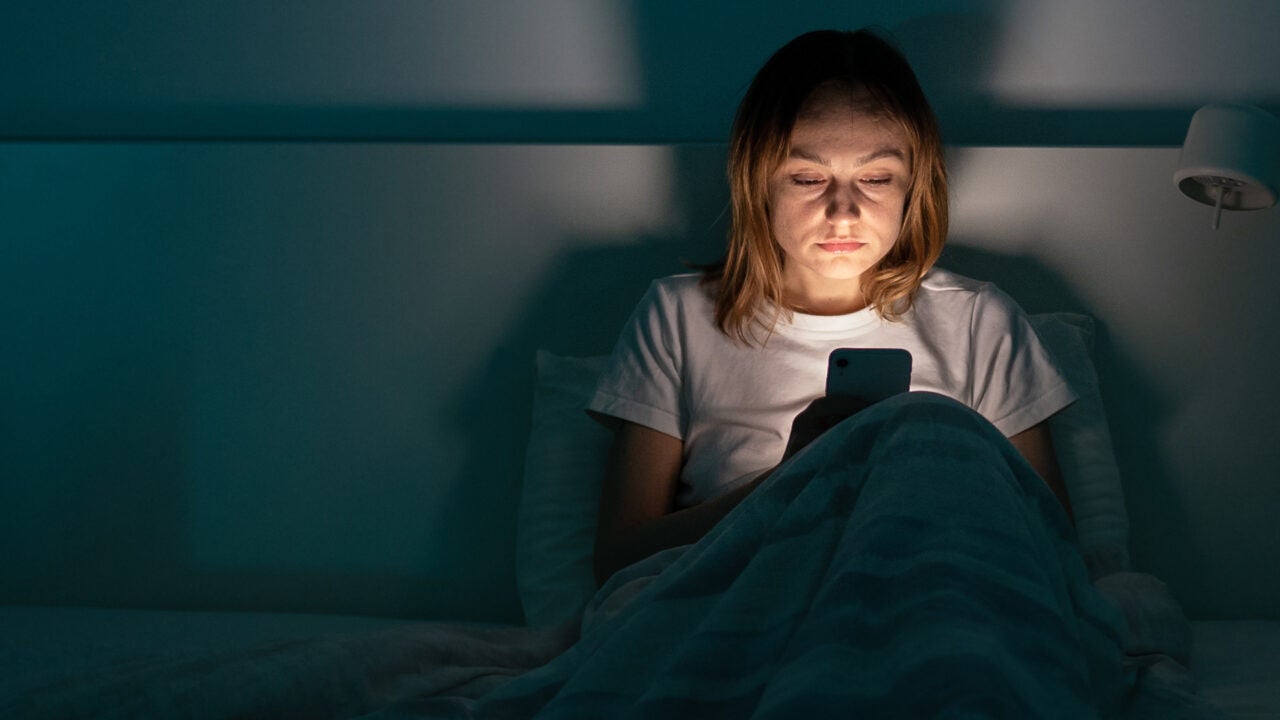 a young woman's face is illuminated by her smart phone as she looks at her phone in a dark room