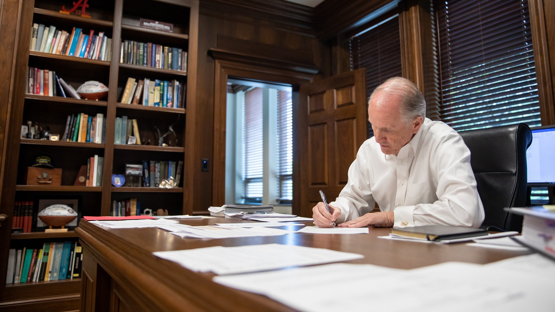 Dr. Bell writes with a pen while sitting as his office desk