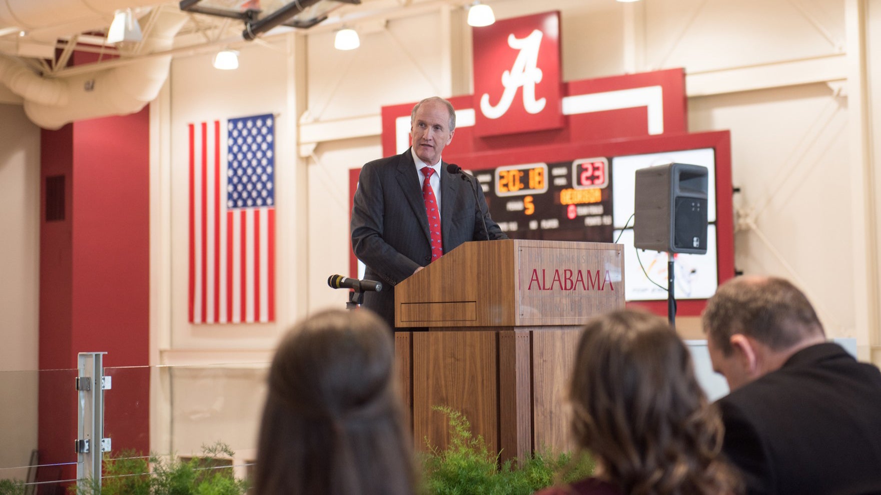 Dr. Bell speaks at a podium in stran hardin arena