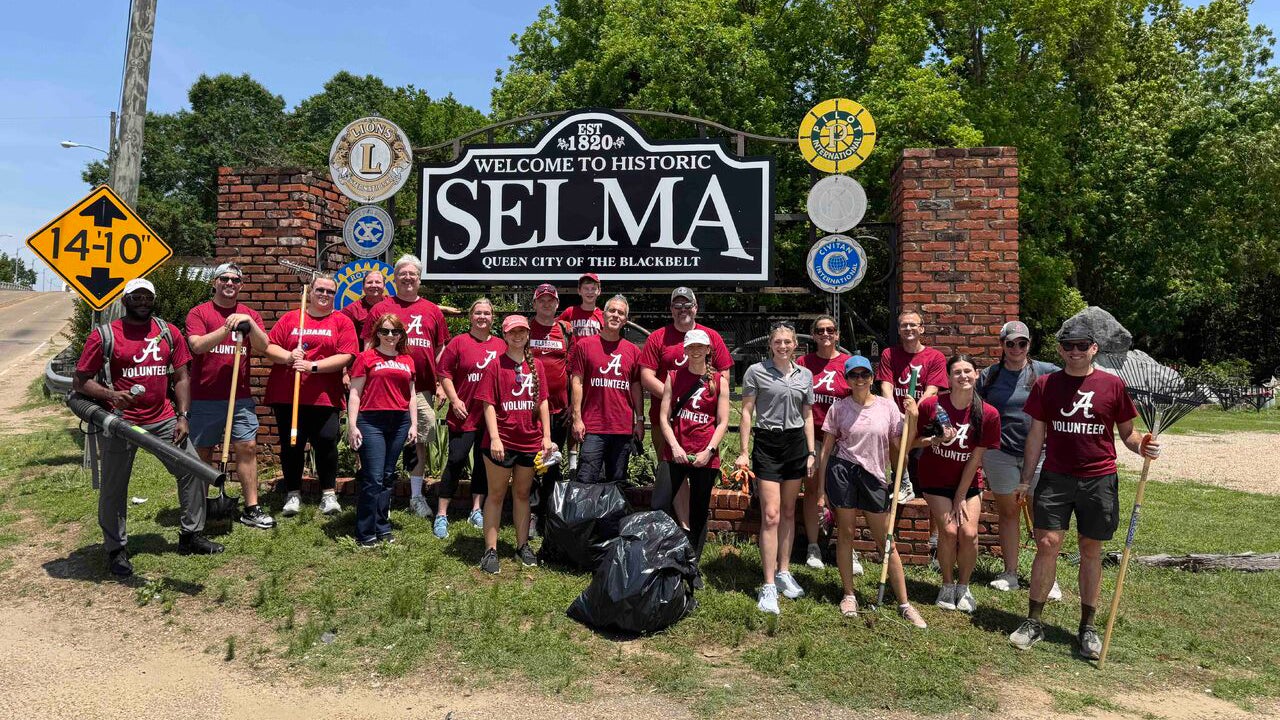 faculty and staff holding rakes and trash bags in front of Selma sign