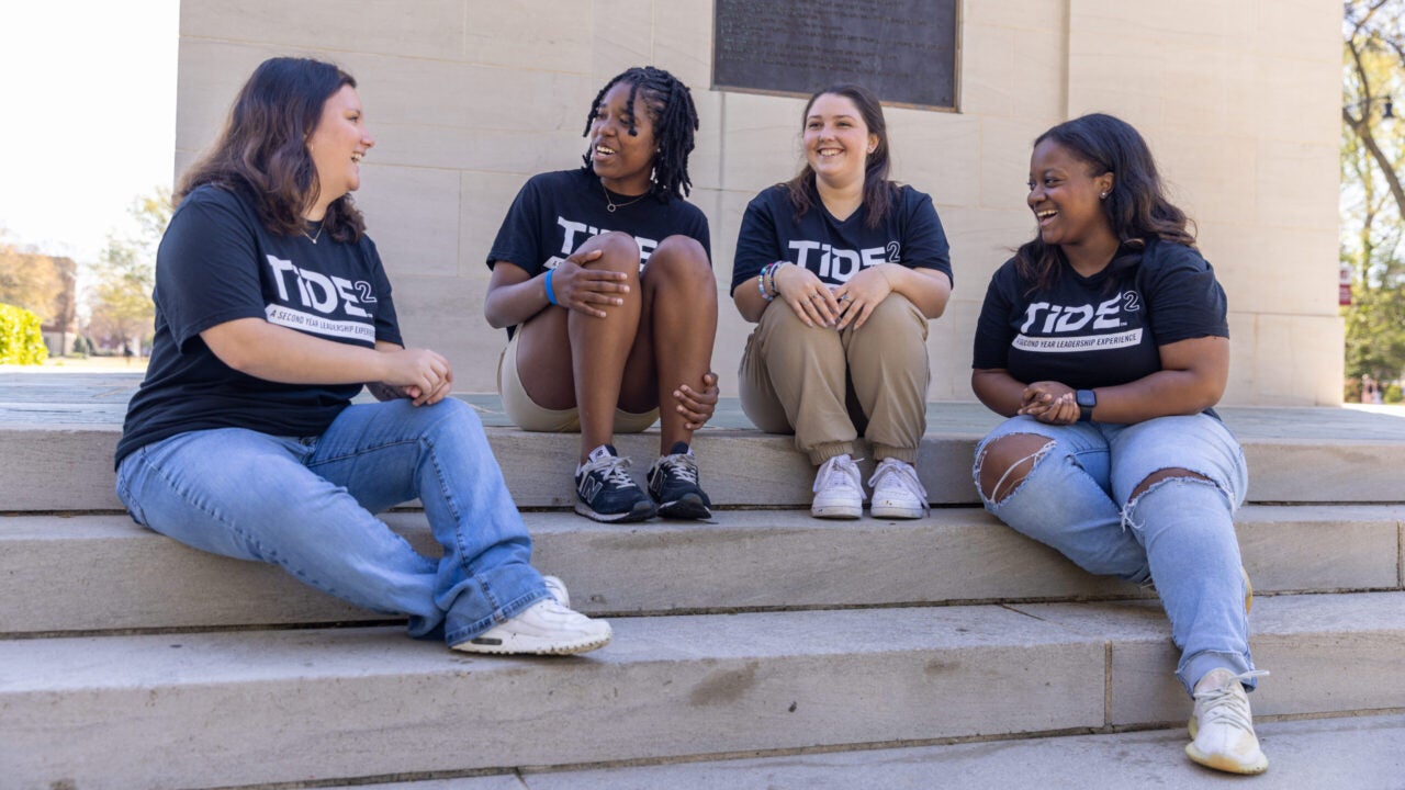 four students sit on the steps of Denny Chimes chatting