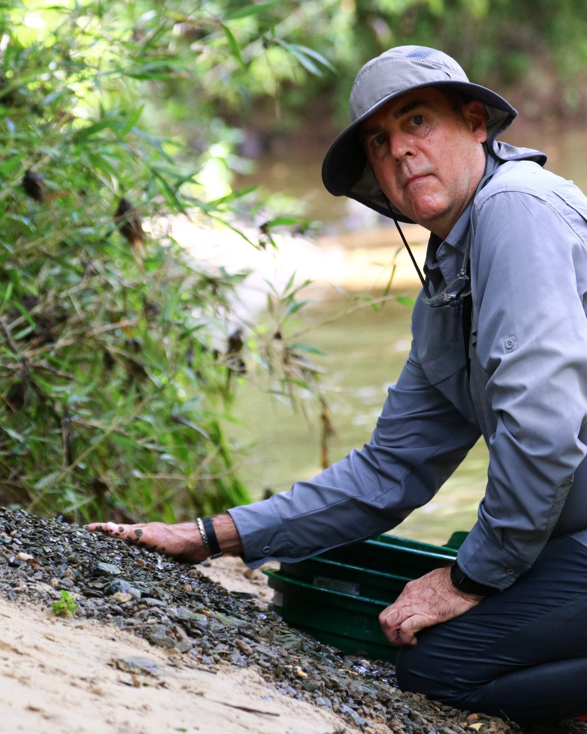 Dr. John Friel, director of the Alabama Museum of Natural History, kneels on the sand. His hand is sifting through the gravel in front of him, looking for fossils and fossilized teeth.