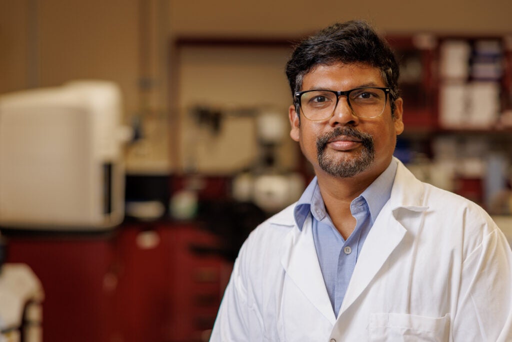 Dr. Raghu Ganugula, wearing a blue shirt and a lab coat, in his lab at the University of Alabama.