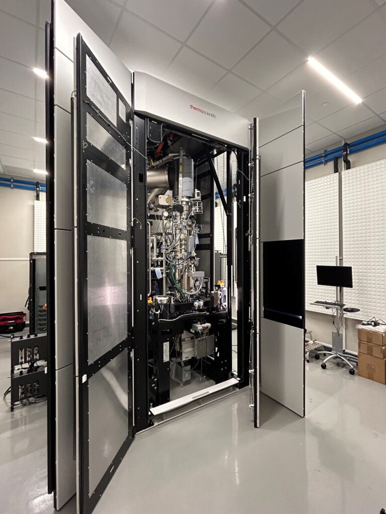 Spectra aberration-corrected transmission electron microscope, a large machine almost the height of the ceiling, in an off-white metal cabinet with the doors open. 