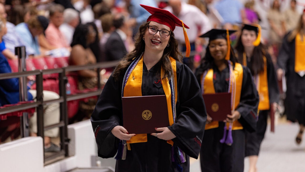 a young women holds her degree and smiles