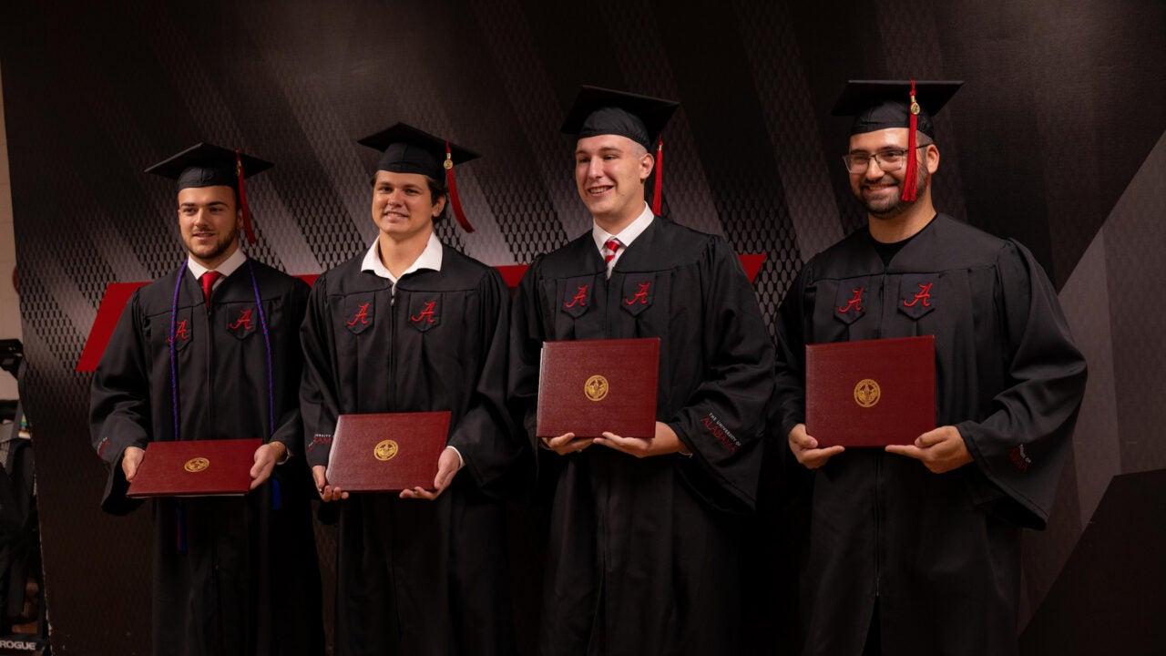 four young men hold up their new degrees