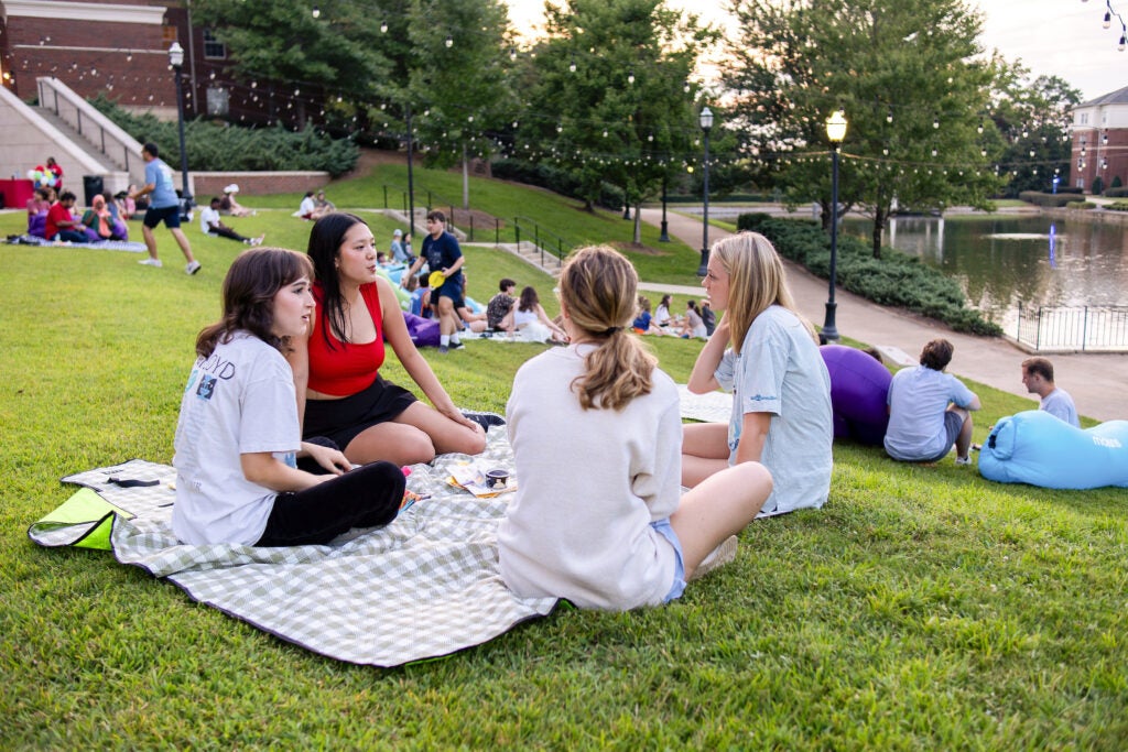 Four students sitting together on a blanket outside.