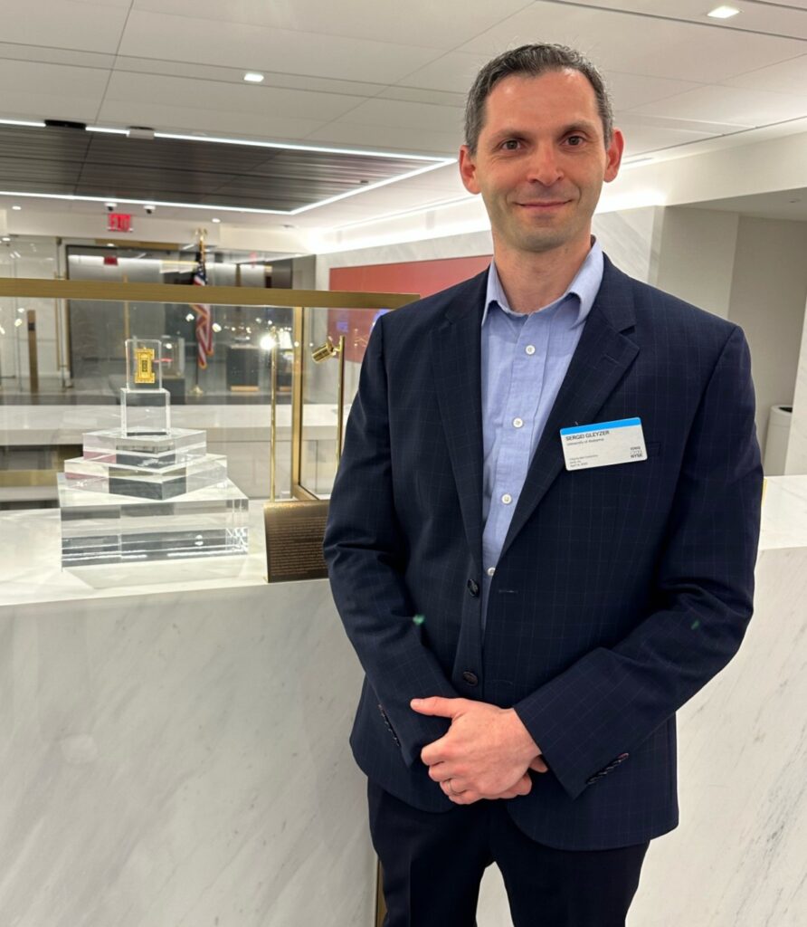 Sergei Gleyzer stands beside a case holding an IonQ quantum chip.