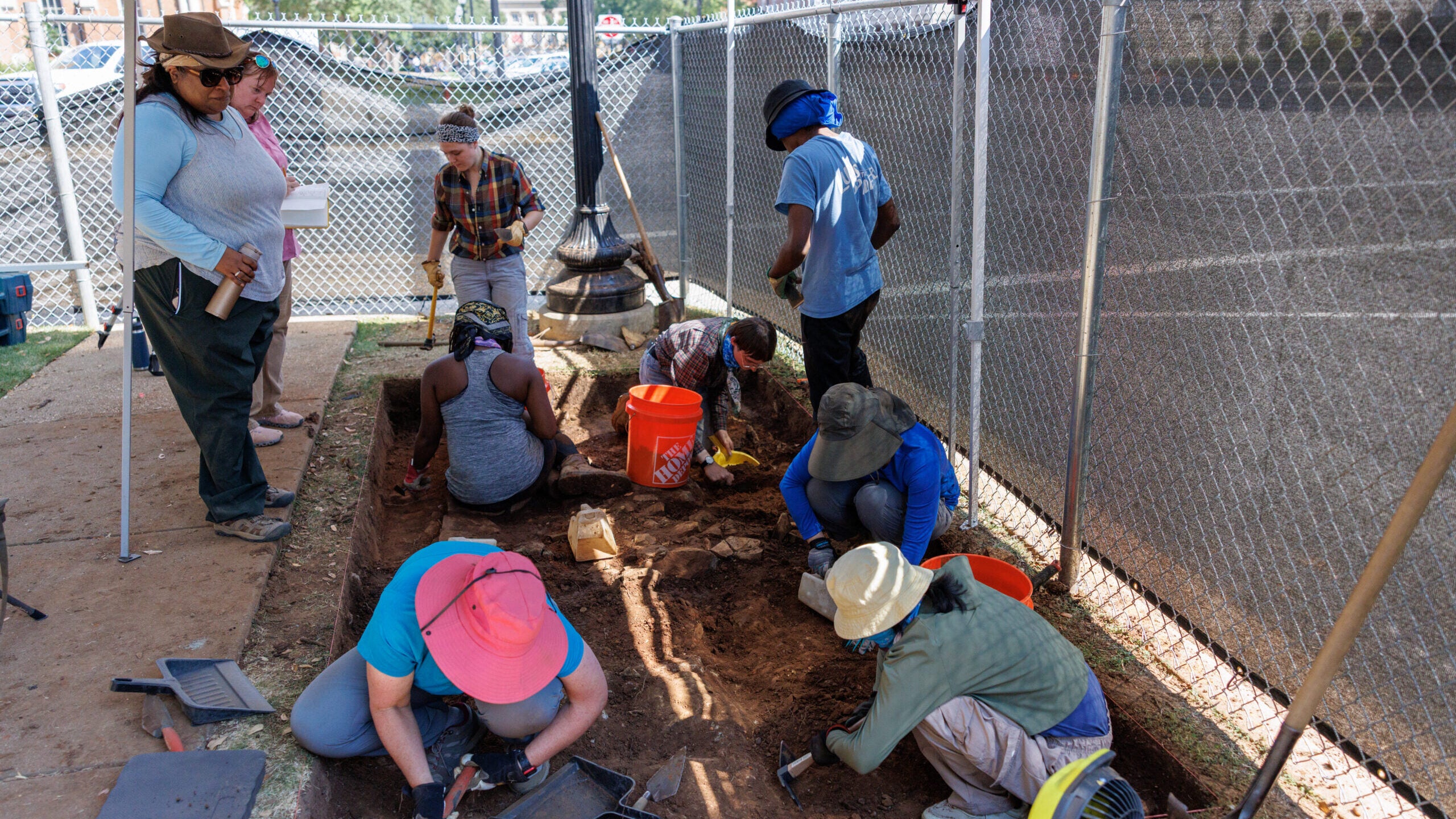 UA students in long pants and work gloves dig and brush away dirt at the archaeological field school on the University of Alabama campus.