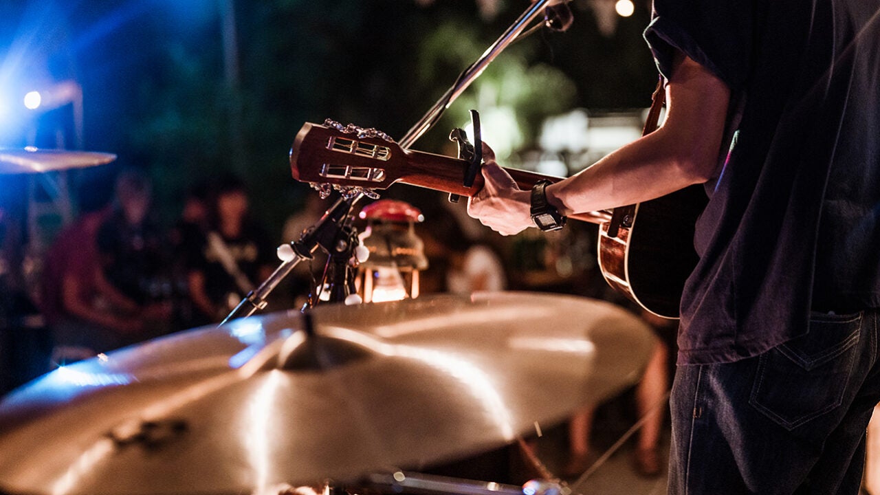 A person plays a guitar around a set of drums.