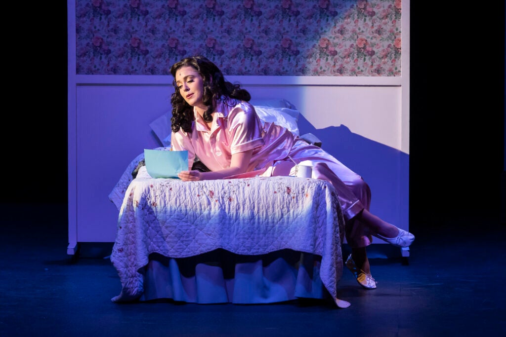 Neeley Robertson lays on a bed reading a letter during a stage play