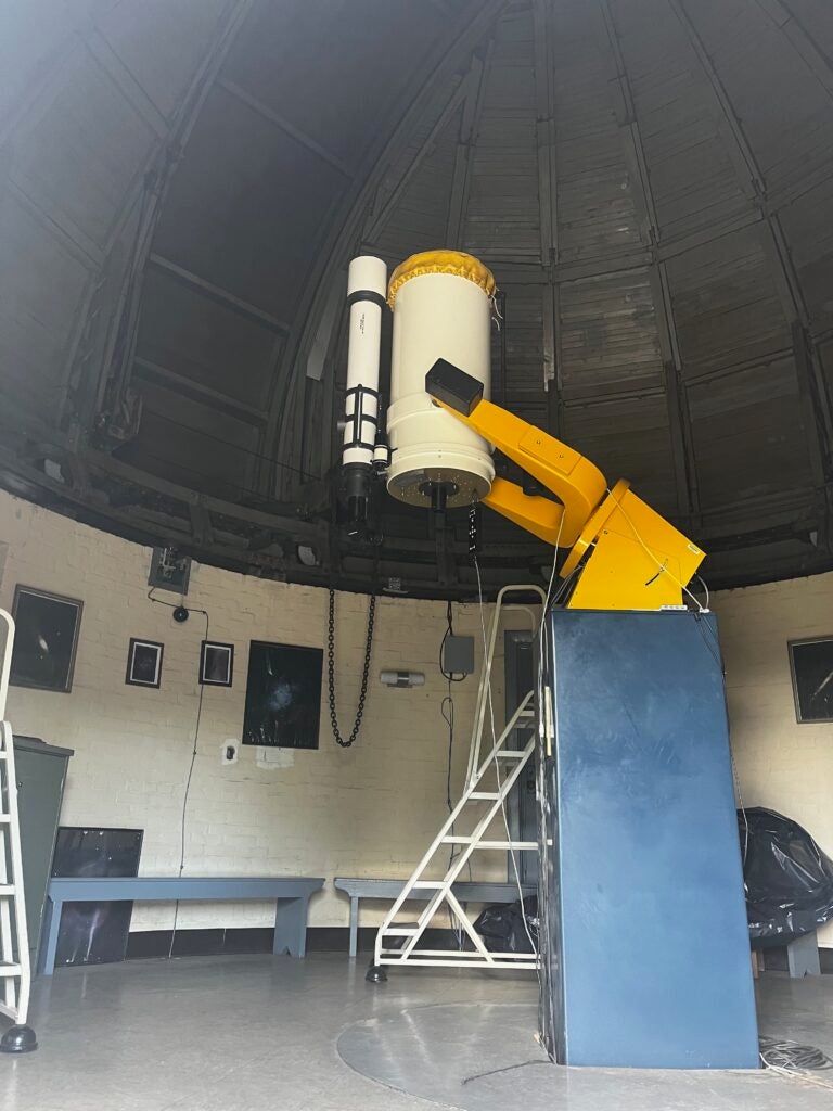 Interior of the UA Gallalee Hall observatory. A large telescop mounted on a metal frame is pointed at the domed roof. 