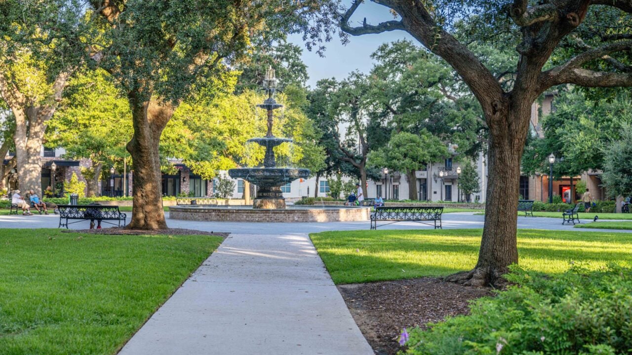 Urban park in downtown Mobile, Ala. Sidewalk flanked by trees leading to a metal foutain.