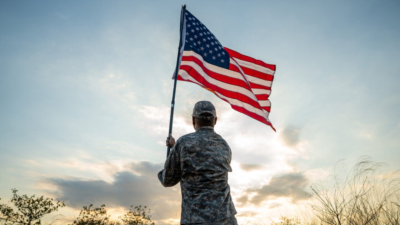 a person in army fatigues waves an American flag