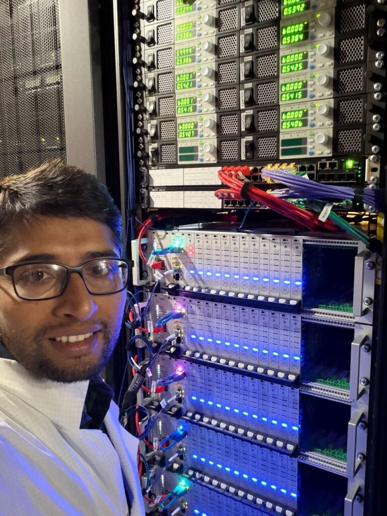 Dr. Ek Narayan Paudel with a wall of machines with blue and green lights.