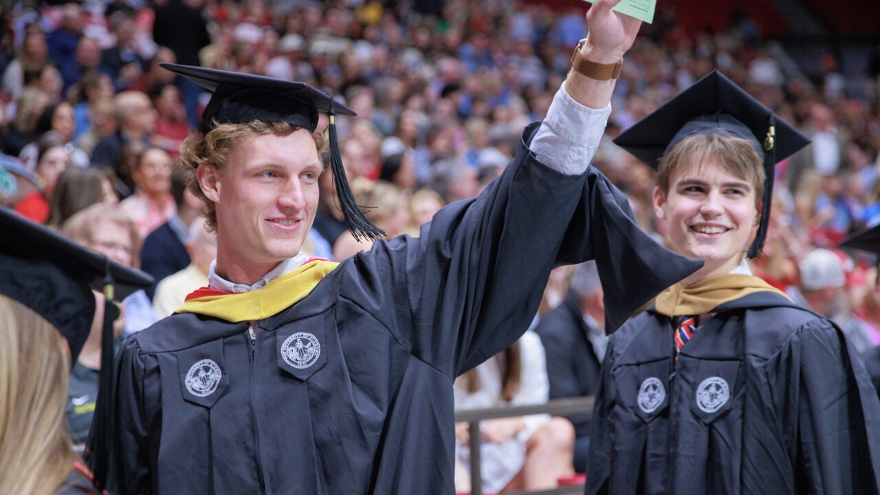 a young man waves to the crowd and smiles while walking to his seat.