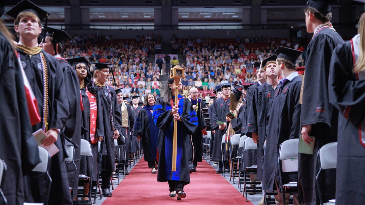 the faculty marshal carries the ceremonial mace down the aisle at commencement