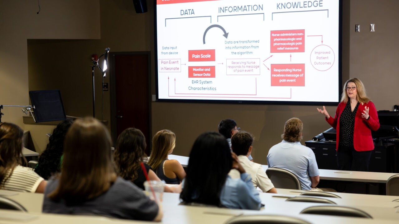 A professor stands in front of her class giving a lecture.