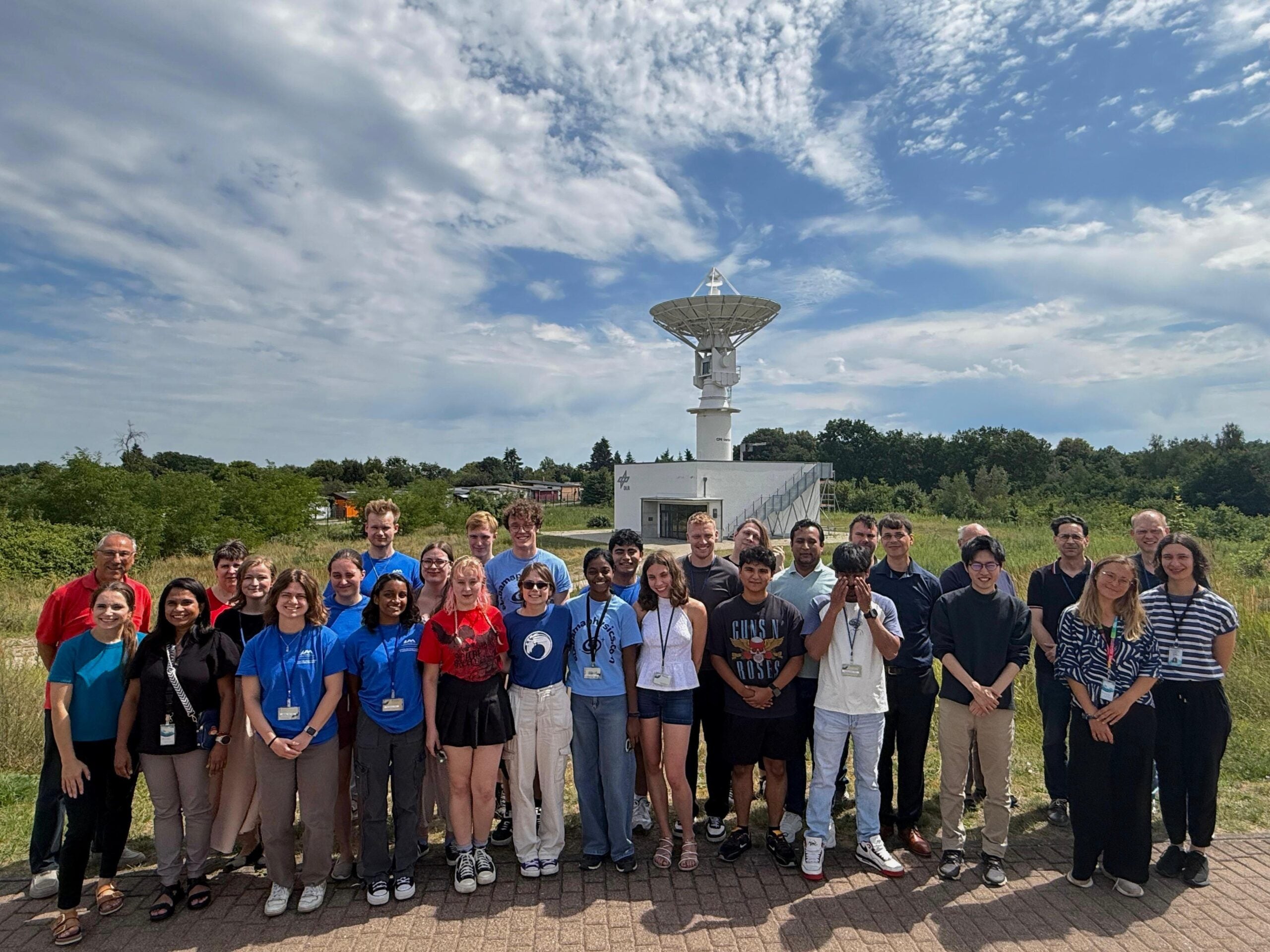 Participants in the International Space Weather Camp stand outdoors for a group photo in front of a satellite antenna at the German Aerospace Center in Neustrelitz, Germany. Fernando Salinas participated in the international research program focused on space weather.
